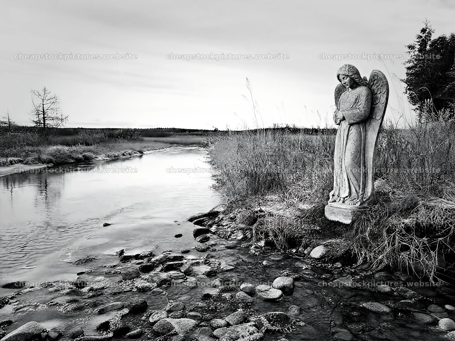 Winter angel statue by the river in a meadow landscape – stock pictures 9166x6874