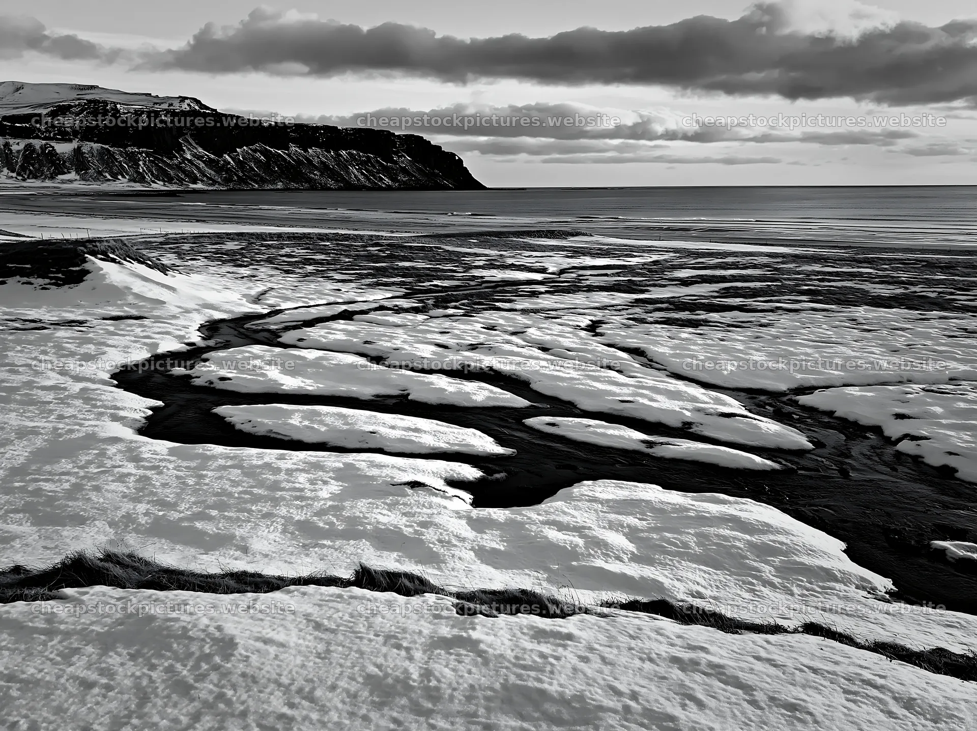 Snowbound meadow with flowing stream and cliffs in background – stock pictures 9174x6866