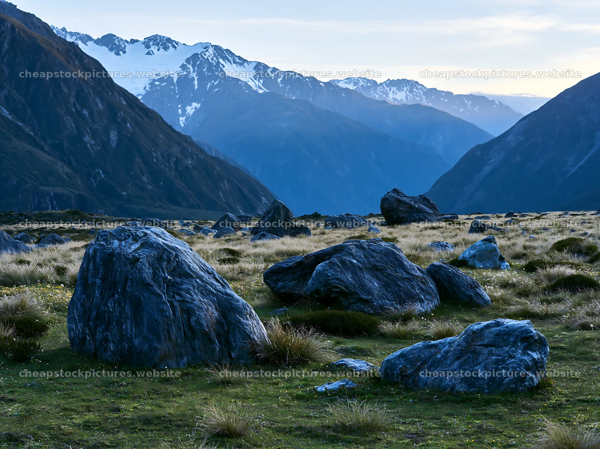 Boulders in a meadow with mountains in the background – stock pictures 9174x6866